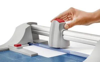 Mano operando una guillotina o cizalla para cortar papel con precisión.