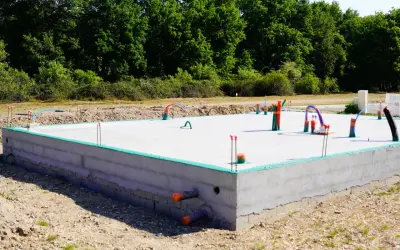 Nowa płyta fundamentowa z wystającymi rurami i instalacjami, gotowa na dalsze prace budowlane.