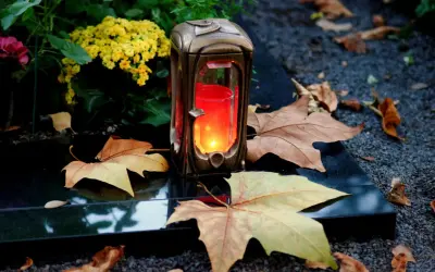 Grablicht auf einem Grabstein, umgeben von Herbstlaub und Blumen. Ein stiller Gruß zu Allerheiligen katholisch.