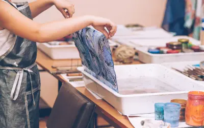 Manos sostienen tela con diseño marmoleado sobre una bandeja con agua, lista para la pintura para mármol.