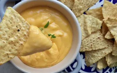 Chrupiące nachos zanurzane w kremowym sosie z serka topionego, ozdobionym gałązką ziół. Idealna przekąska!