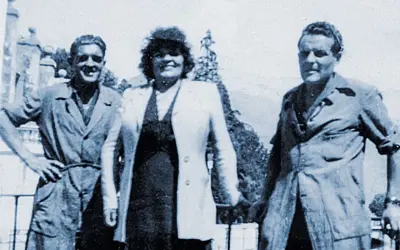 Trois personnes posent devant un paysage. L'homme de gauche, peut-être le fondateur Millet, sourit.