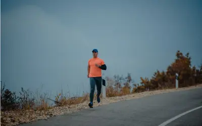 Mężczyzna w pomarańczowej koszulce i czapce biega po pustej drodze. Czy można biegać na czczo? To pytanie zadaje sobie wielu sportowców.