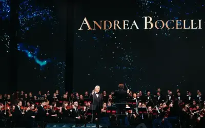 Andrea Bocelli koncert 2026. Wokalista śpiewa z orkiestrą symfoniczną na tle gwieździstego nieba.