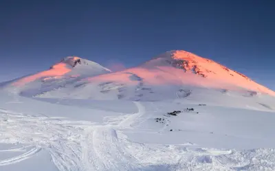 Śnieżne szczyty najwyższego wulkanu w Europie, Elbrusu, skąpane w różowym blasku wschodzącego słońca.