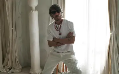Pierpaolo Piccioli, con occhiali da sole e collane, posa con le braccia conserte in un ambiente chiaro con tende e colonne.