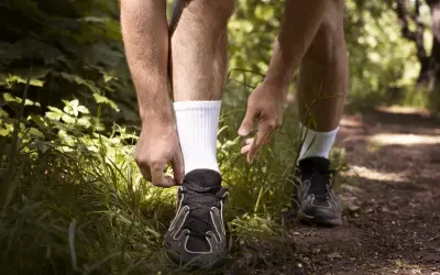 Biegacz przygotowuje się do treningu, sznurując buty. Dobre **jakie skarpetki do biegania** to podstawa komfortu na leśnej ścieżce.