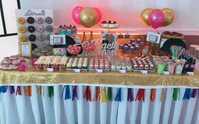 Słodki stół z donutami, babeczkami i deserami w słoiczkach, jak na wesele lata 80. Złoty obrus i kolorowe balony dodają blasku.