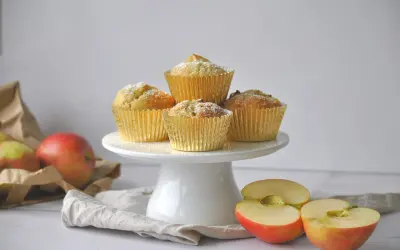 Goldene Muffins mit Puderzucker, daneben Äpfel und eine Tüte. Ein leckeres apfelmuffins rezept zum Nachbacken.