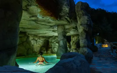 Una mujer disfruta de un relajante spa de noche en una piscina natural rodeada de rocas.