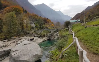 Sentiero sul monte Valdo, con un ponte ad arco in pietra, un fiume turchese e montagne sullo sfondo.