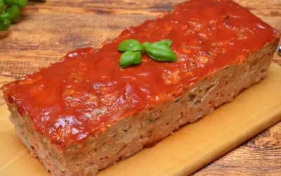 Pyszny, domowy meatloaf z sosem pomidorowym i listkami bazylii, gotowy do podania na desce.
