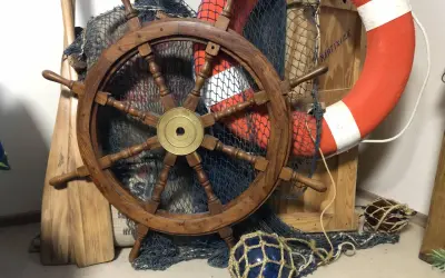 Roue de gouvernail en bois, filet de pêche, bouée de sauvetage orange et pagaies évoquent un safran de bateau prêt pour l'aventure.