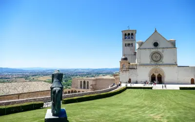 Statua equestre domina il prato verde di Assisi. Cosa vedere: la Basilica di San Francesco, con la sua imponente facciata e campanile, si staglia contro il cielo azzurro.