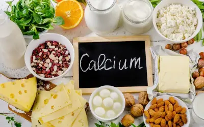 Talerzyk z serem, fasolą, orzechami, migdałami, pomarańczą i nabiałem. Na tablicy napis "Calcium".