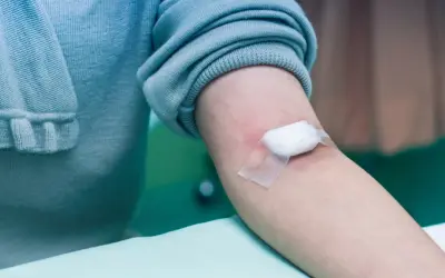 Ramię z wacikiem i plastrem po pobraniu krwi, czekając na wyniki badań.