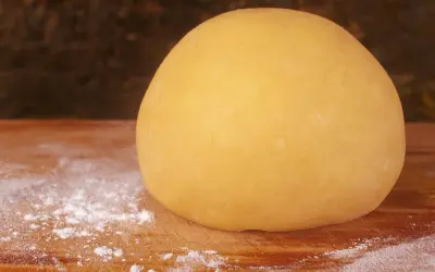 Impasto di pasta frolla per pastiera, 1 kg, pronto per essere steso su un tagliere infarinato.