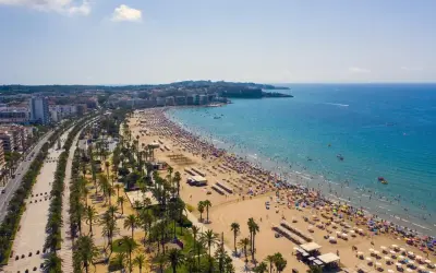 Tłum ludzi cieszy się słońcem na plaży, a w tle widać miasto. To idealne miejsce na wakacje, pełne atrakcji Costa Dorada.