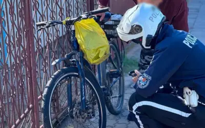 Policjant sprawdza rower na drodze dla rowerów. Żółta torba wisi na kierownicy.