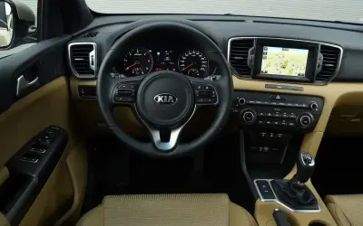 Wnętrze Kia Sportage IV z beżową tapicerką, multimediami z nawigacją i wielofunkcyjną kierownicą.