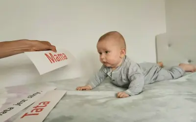 Uroczy noworodek na brzuchu, zaciekawiony kartkami z napisami "Mama" i "Tata".