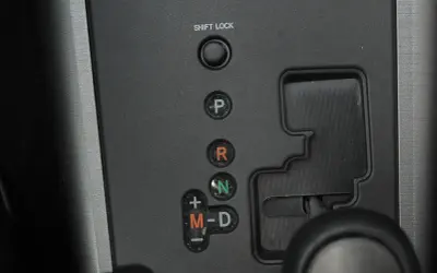 Panel z przyciskami skrzyni biegów: P, R, N, M-D. Obok przycisku "SHIFT LOCK" znajduje się otwór do jego zwolnienia.