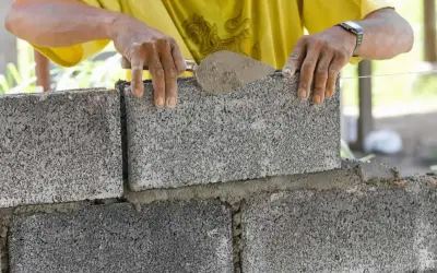 Murarz układa bloczek betonowy, dbając o jego wymiary i równość.