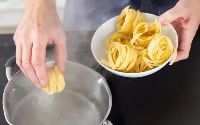 Ręka wkłada porcję tagliatelle do wrzącej wody. Czy makaron gotujemy pod przykryciem? Zobacz, jak zacząć gotowanie.