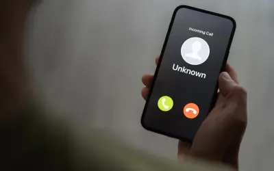 Dłoń trzyma smartfon z ekranem pokazującym przychodzące połączenie od nieznanego numeru. Czy to kolejny **wangiri**?