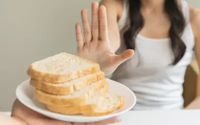 Osoba odrzuca talerz z chlebem, pokazując dłoń. To symbol walki z celiakią i unikania glutenu.