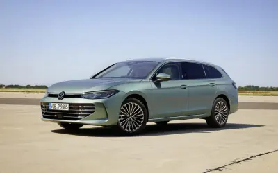 Nowy Volkswagen Passat B9 w kolorze zielonym, zaparkowany na betonowej nawierzchni, z błękitnym niebem w tle.