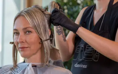 Une coiffeuse applique une couleur ou une mèche pour cacher les cheveux blancs d'une cliente.