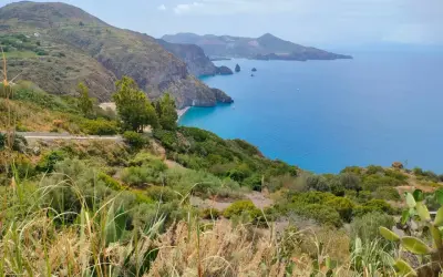 Panoramica mozzafiato per capire come visitare le Isole Eolie: costa verdeggiante, mare blu intenso e isole vulcaniche all'orizzonte.