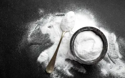 Un cucchiaio e una ciotola pieni di carbonato di sodio, mostrando i suoi molteplici usi in cucina e per la pulizia.
