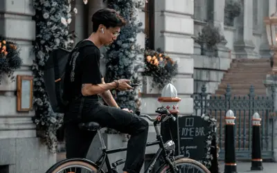 Jonge man op fiets met rugzak, kijkend op zijn telefoon. Is een fietser altijd beschermd in het verkeer?