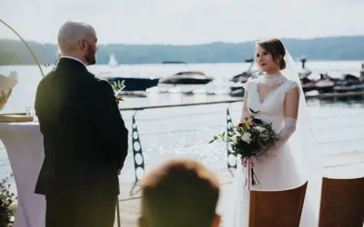 Panna młoda z bukietem w dłoniach patrzy na pana młodego. To ich ślub jednostronny nad jeziorem.