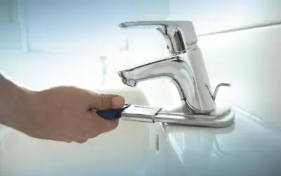 Mano con chiave per cambiare rubinetto lavandino bagno.