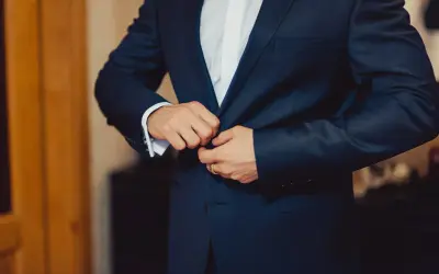 Mężczyzna zapina elegancki, granatowy **strój formalny**. Widać białą koszulę i mankiet z francuskimi spinkami.