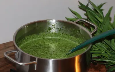 En kastrull med grön spenatsoppa, redo för ett enkelt spenatsoppa recept. Gröna blad syns i bakgrunden.
