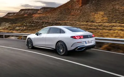 Weißer Mercedes C-Klasse EQ fährt auf einer Straße in bergiger Landschaft.