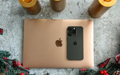 Złoty MacBook i czarny iPhone na tle świątecznych dekoracji. Idealny zestaw do pracy i rozrywki z macOS.