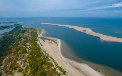 Piękna wycieczka nad morze. Piaszczysta mierzeja otoczona wodą, z zielenią po lewej stronie.