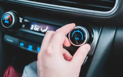 En hand vrider på reglaget för ac i bilen. Temperaturen sjunker snabbt.