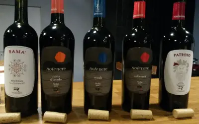 Pięć butelek wina, w tym dwie z etykietą "note nere nero d'avola sicilia doc", stoją na drewnianym stole.
