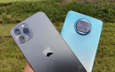Porównanie aparatów: iPhone (iOS) kontra Xiaomi (Android). Dwa smartfony na tle zielonej trawy.