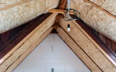 Dämmmaterial wird in einem Dachboden verlegt, um das Haus zu isolieren. Holzbalken und Kabel sind sichtbar.