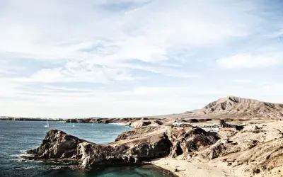 Surowe krajobrazy wulkaniczne Lanzarote, gdzie skutki braku zapasu wody są widoczne na trasach turystycznych, kontrastują z błękitem oceanu i białymi żaglami.