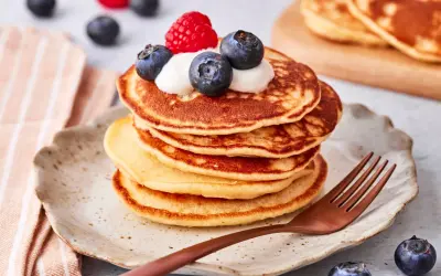 Ein Stapel goldbrauner Pancakes mit Joghurt, Blaubeeren und einer Himbeere obendrauf. Ein köstlicher pancake mit joghurt für ein perfektes Frühstück.