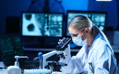 Diagnosta laboratoryjny w okularach i masce pochyla się nad mikroskopem, analizując próbki.