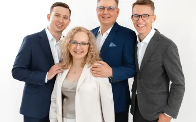 Cztery osoby w eleganckich strojach, uśmiechnięte, na białym tle.